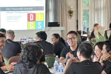 Participants engaging in a DISC Personality Exercise workshop, with a presentation screen displaying "DISC" and presenters' names, highlighting team-building and communication enhancement.
