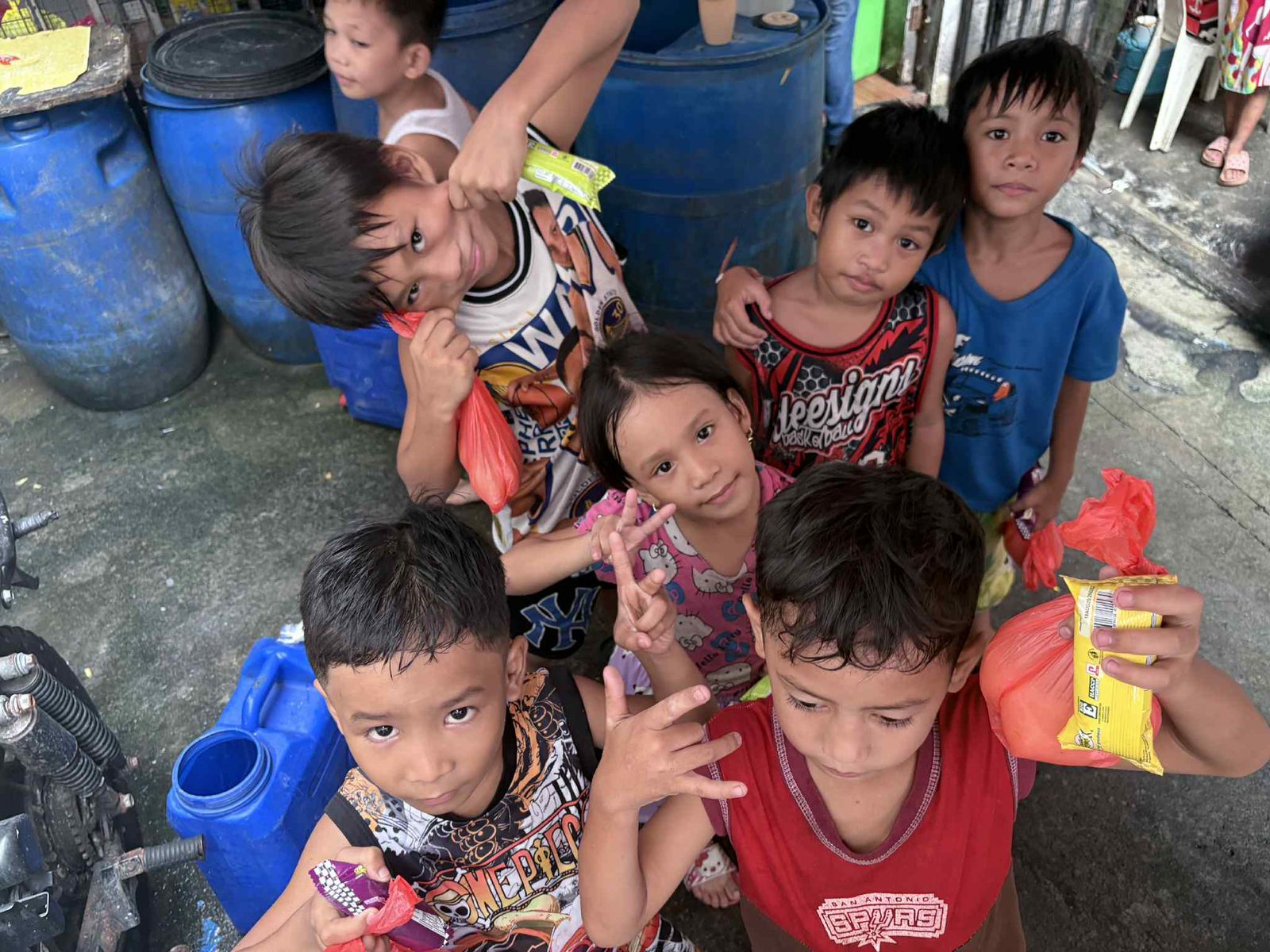 Children in Tondo, Manila, holding food packages and smiling, surrounded by barrels, highlighting the community's struggle with poverty and the impact of CSR initiatives.