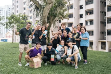 A diverse group of people smiling and posing outdoors near residential buildings.