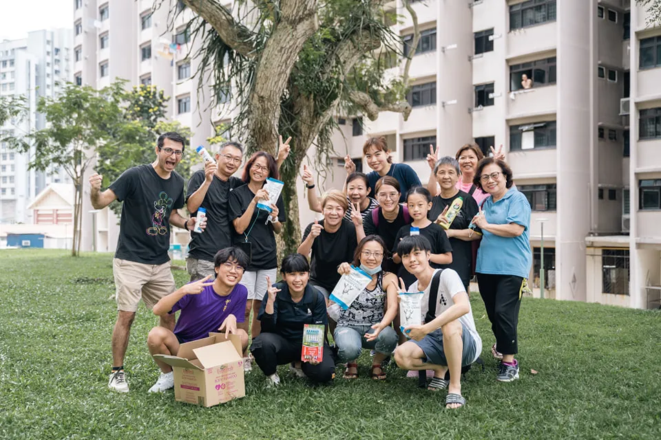 A diverse group of people smiling and posing outdoors near residential buildings.