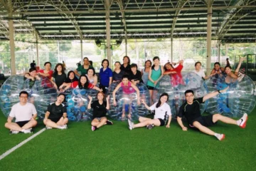 Group of people in inflatable bubble suits on a grassy field.