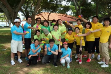 Group of people in colorful shirts holding water guns, posing in a park.
