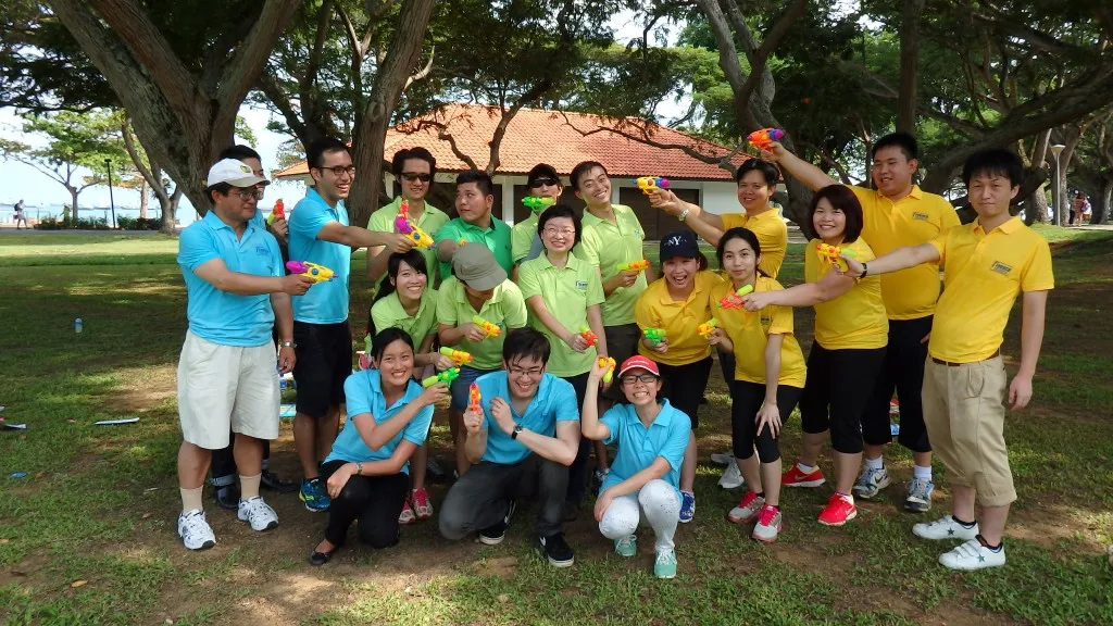 Group of people in colorful shirts holding water guns, posing in a park.