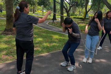 Two people playfully interacting with a rope in a green park setting