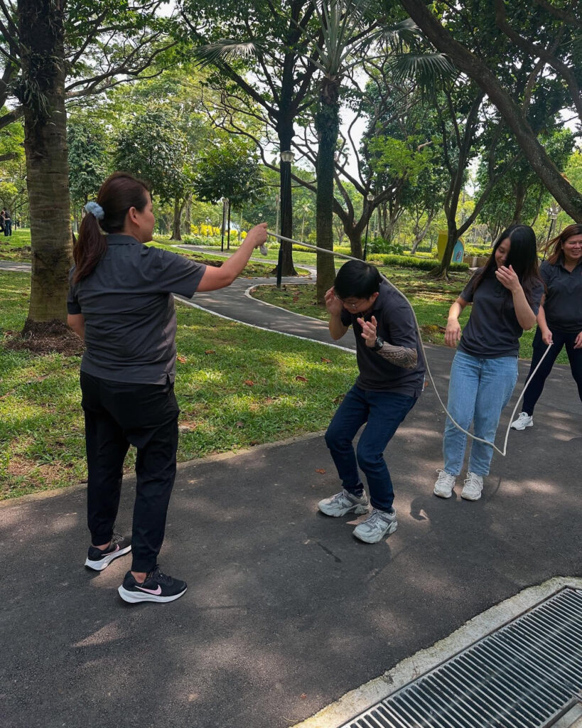 Two people playfully interacting with a rope in a green park setting