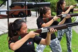 Three women aiming shotguns at a shooting range with cannons in the background