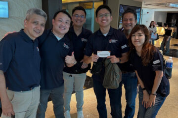 Six people in matching navy polo shirts posing happily indoors