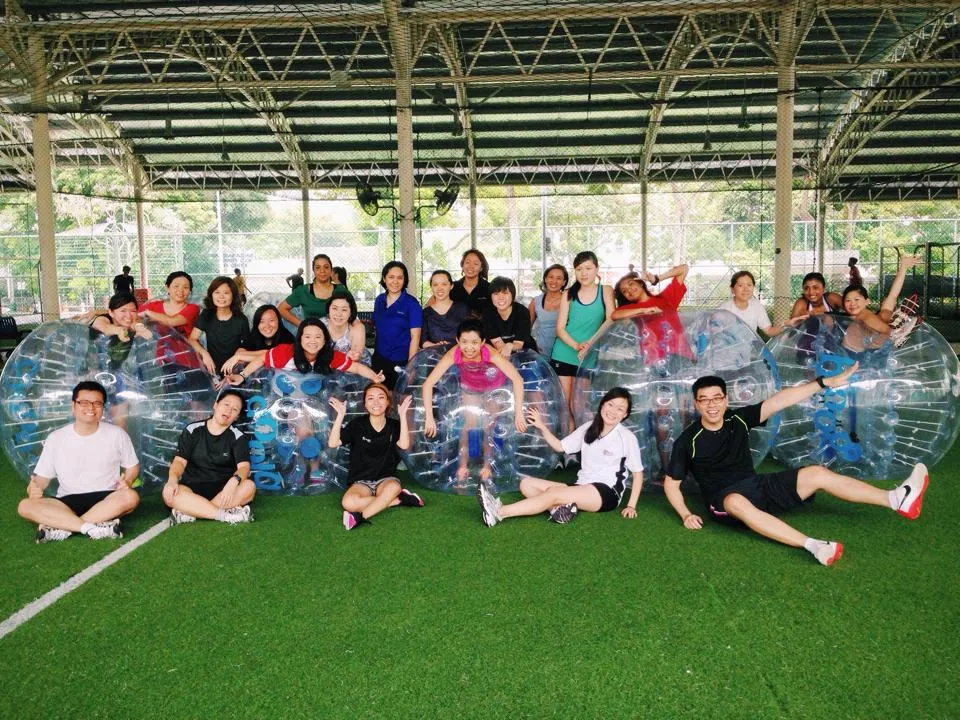 Group of people in inflatable bubble suits on a grassy field.